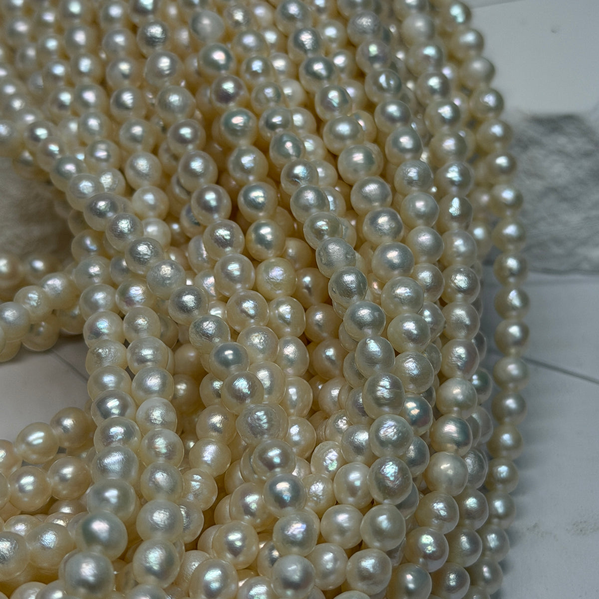 Multiple strands of near round white freshwater pearls draped over a light gray surface.