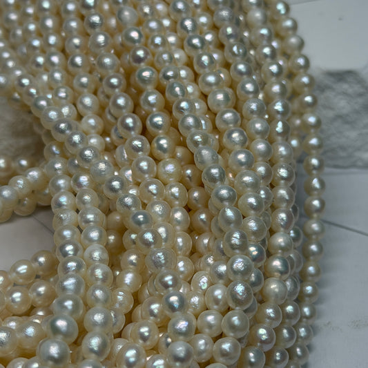 Multiple strands of near round white freshwater pearls draped over a light gray surface.