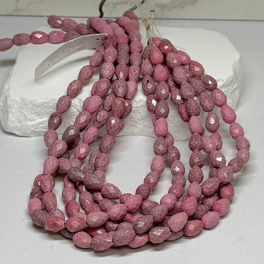 Several strands of faceted, teardrop-shaped dusty pink Rhodonite gemstone beads draped over a white display stone.