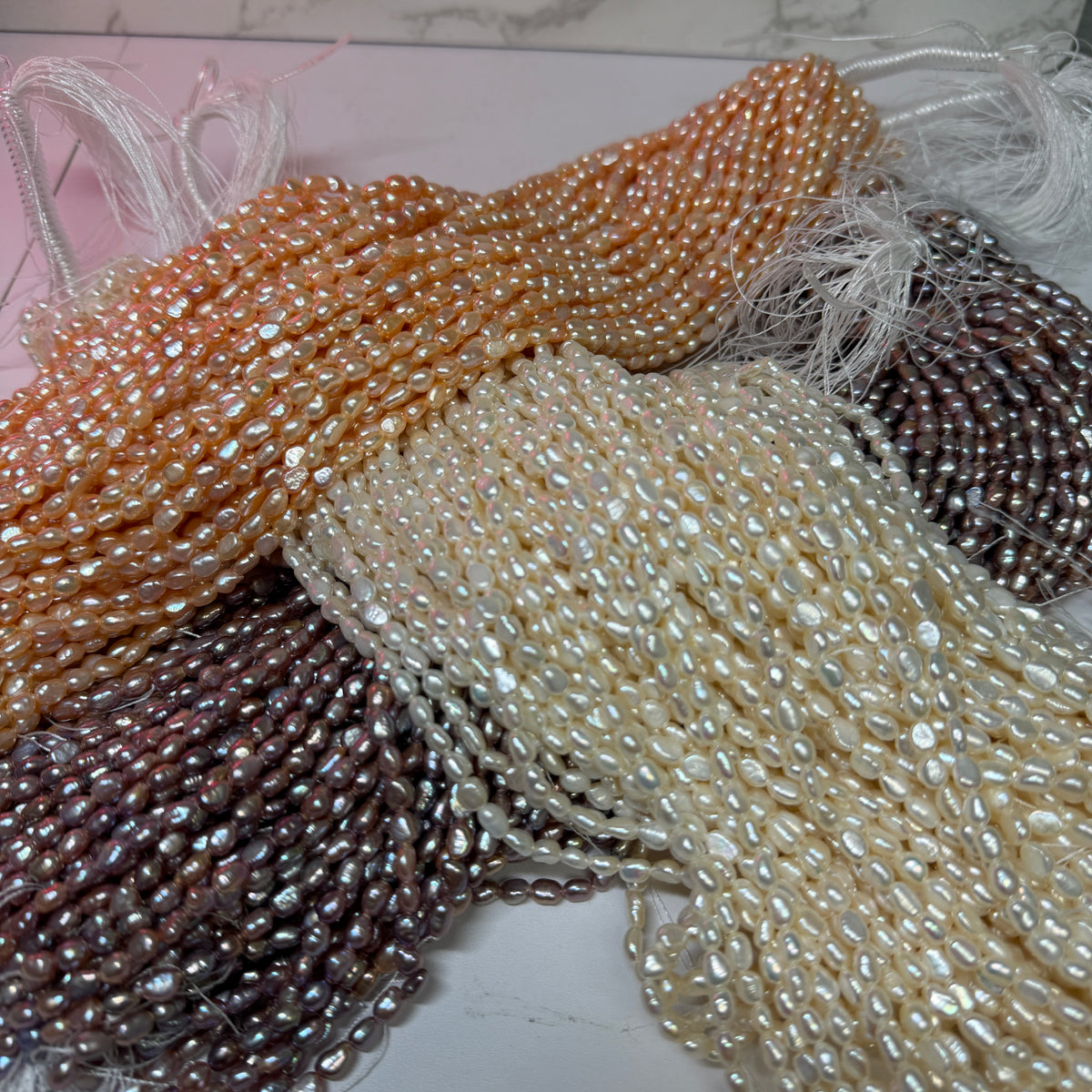Close-up of strands of irregular baroque pearls in multiple colors, including lavender, cream, and peach, laid out over each other.