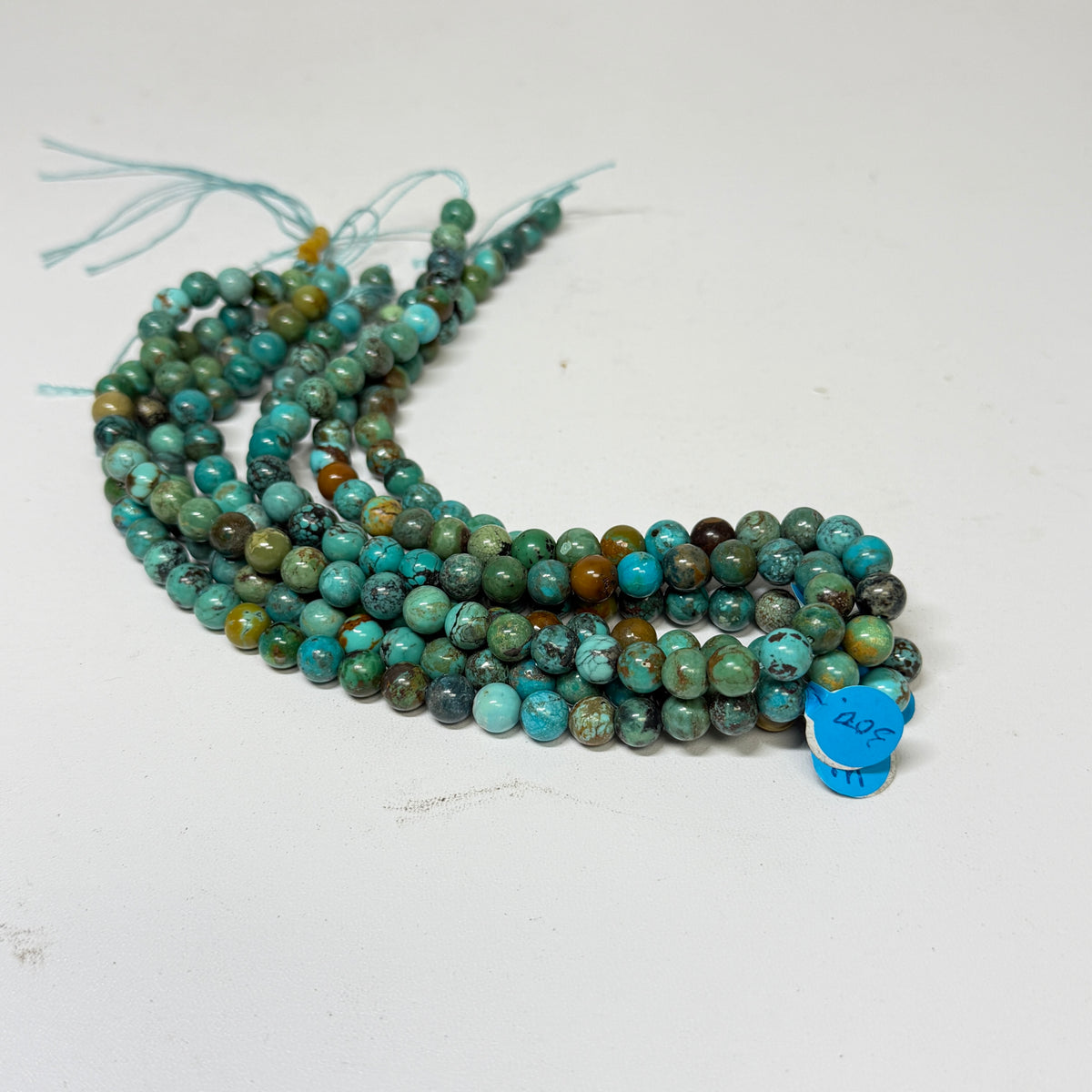 Four strands of round turquoise beads with a small blue price sticker that says 300, displayed on a plain white surface.