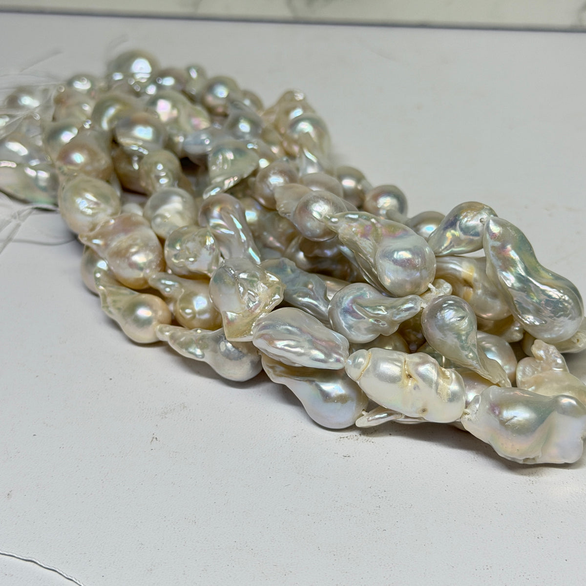 A pile of natural baroque freshwater pearls with an iridescent luster, resting on a light gray surface.