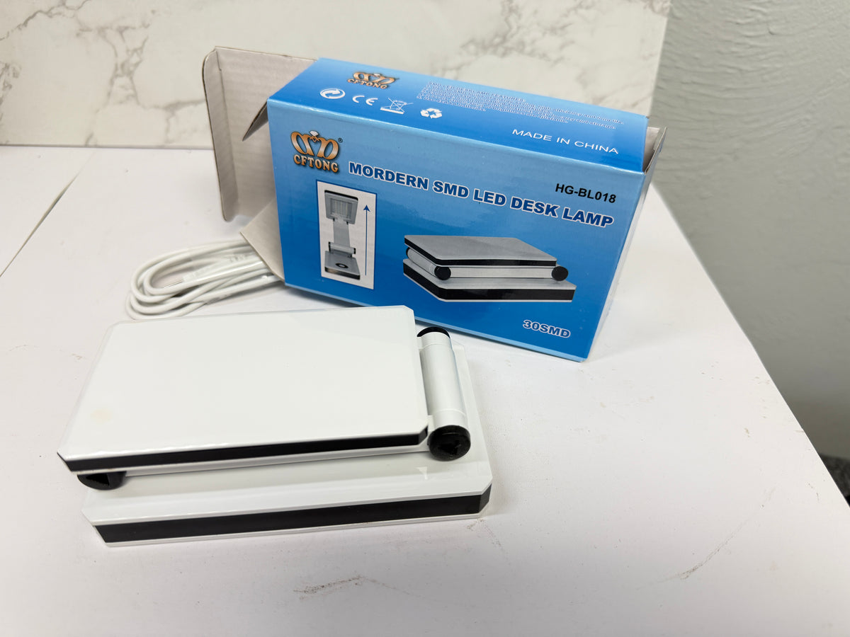 White portable LED desk lamp folded flat beside its USB power cable and blue retail box