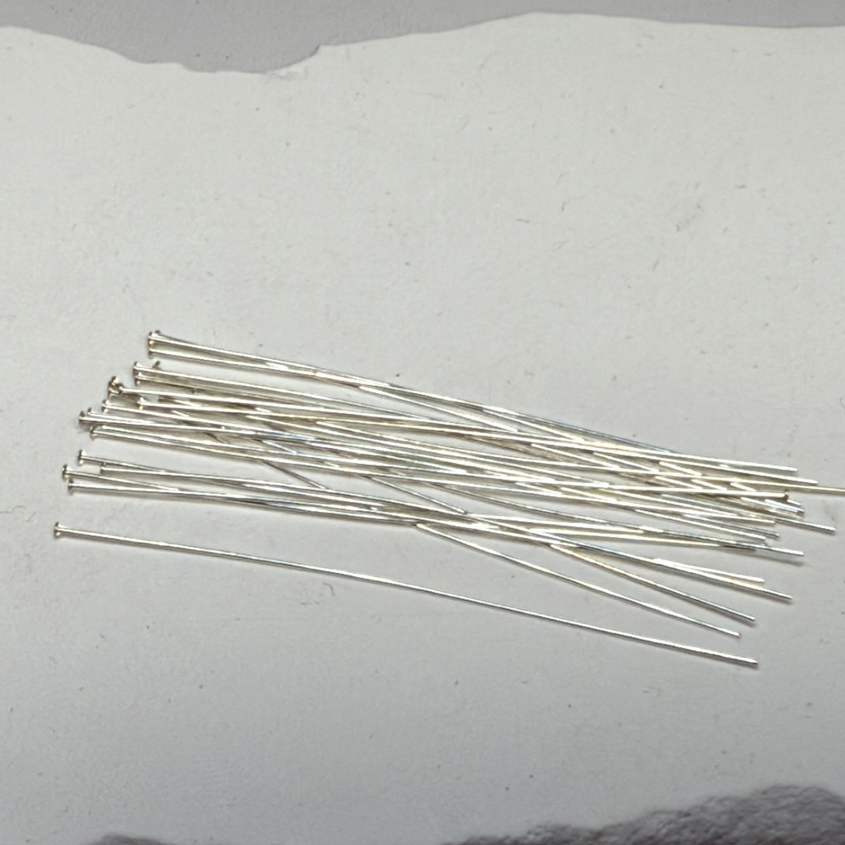 Pile of 26-gauge sterling silver headpins with flat heads, scattered on a white surface."