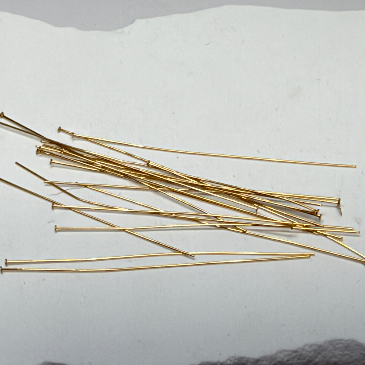 Overlapping gold-filled headpins with slender wire shafts and small flat heads on a white background