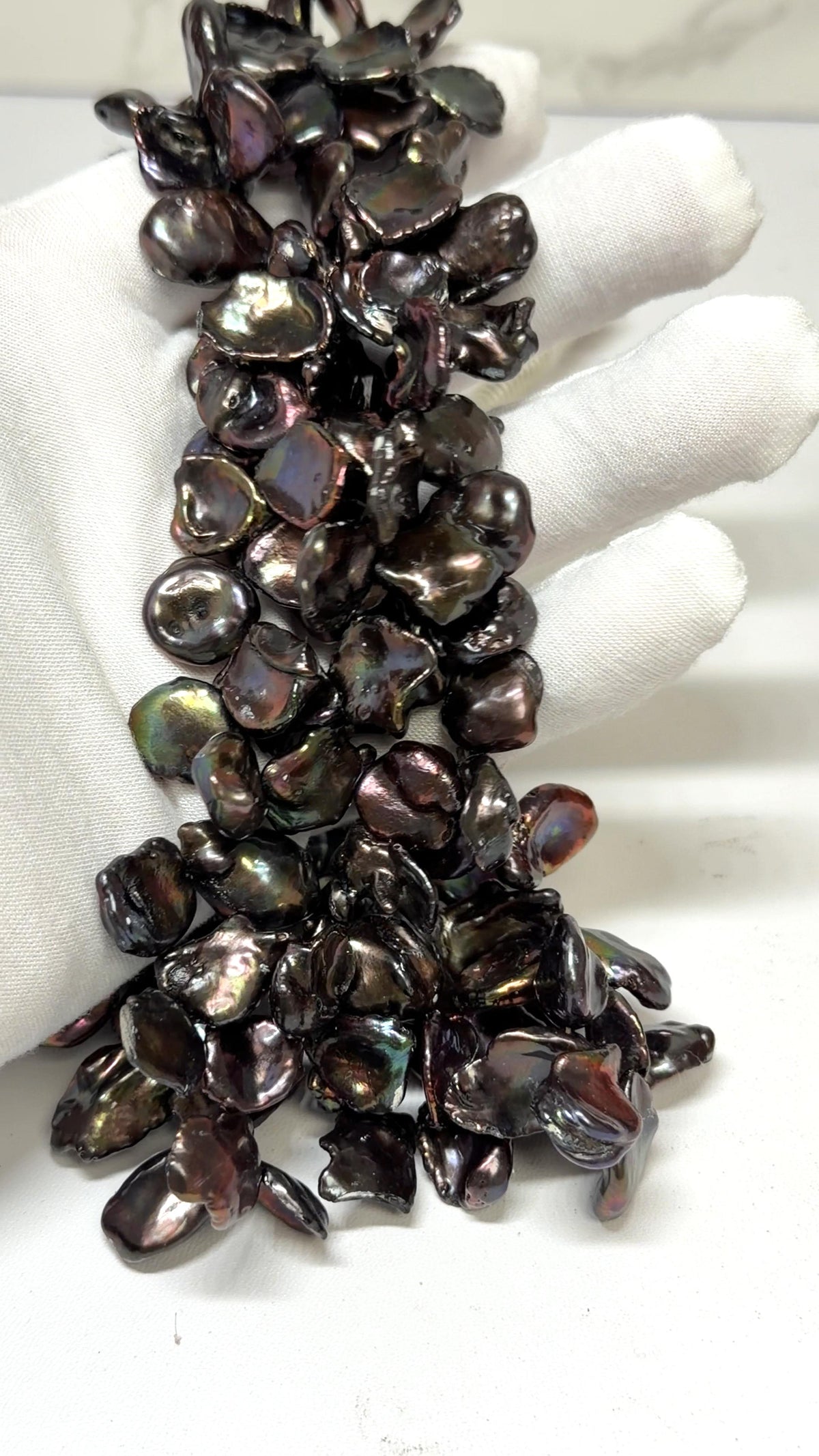 Keshi Peacock pearl strands draped over a white glove