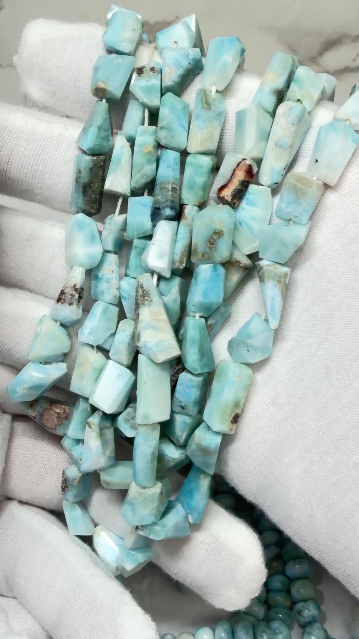 Larimar Freeform Faceted Bead Strands Draped over white gloved hands
