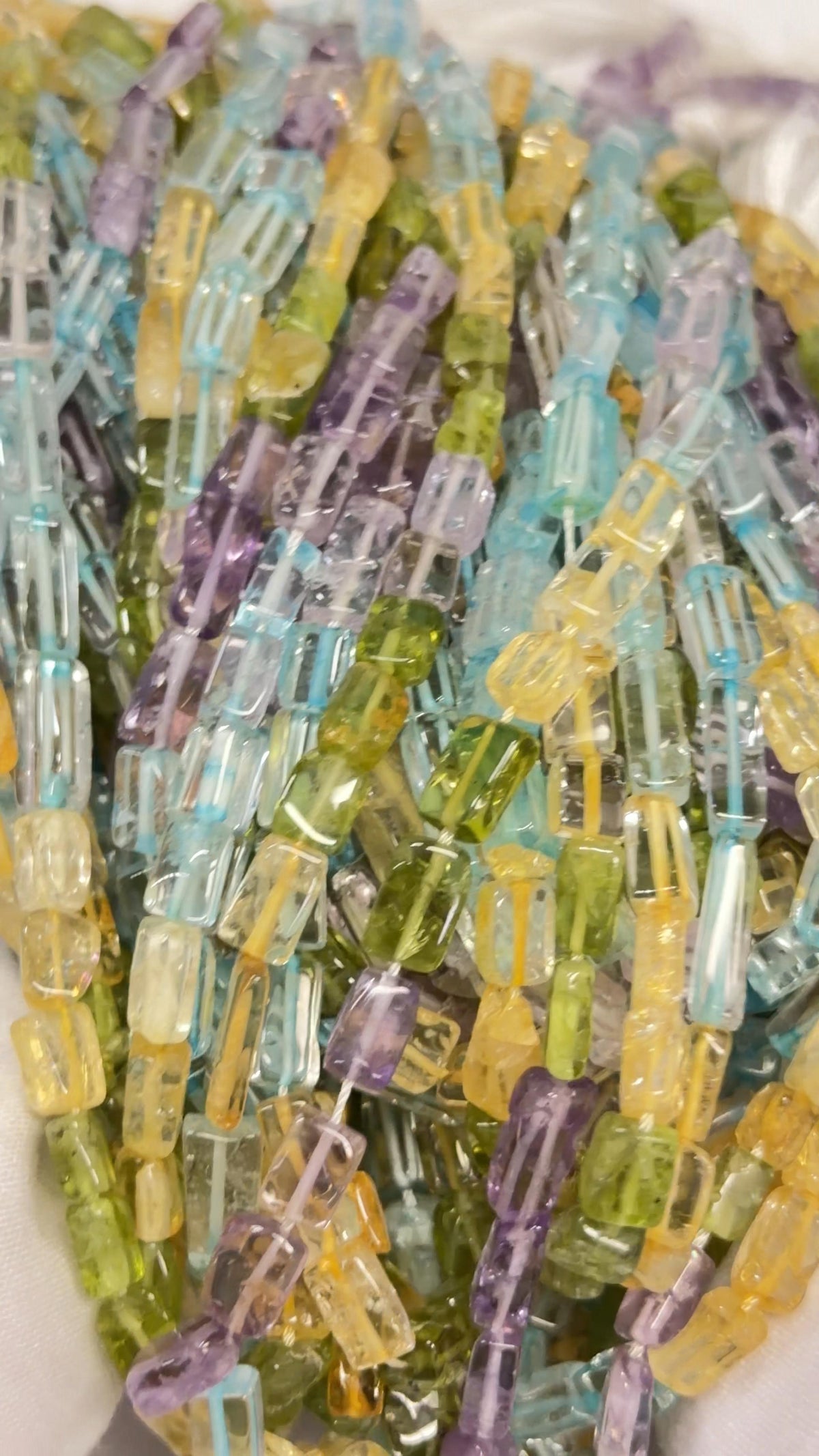 “Close-up of rectangular mixed gemstone bead strands in purple, pale blue, yellow, green, and clear tones.”