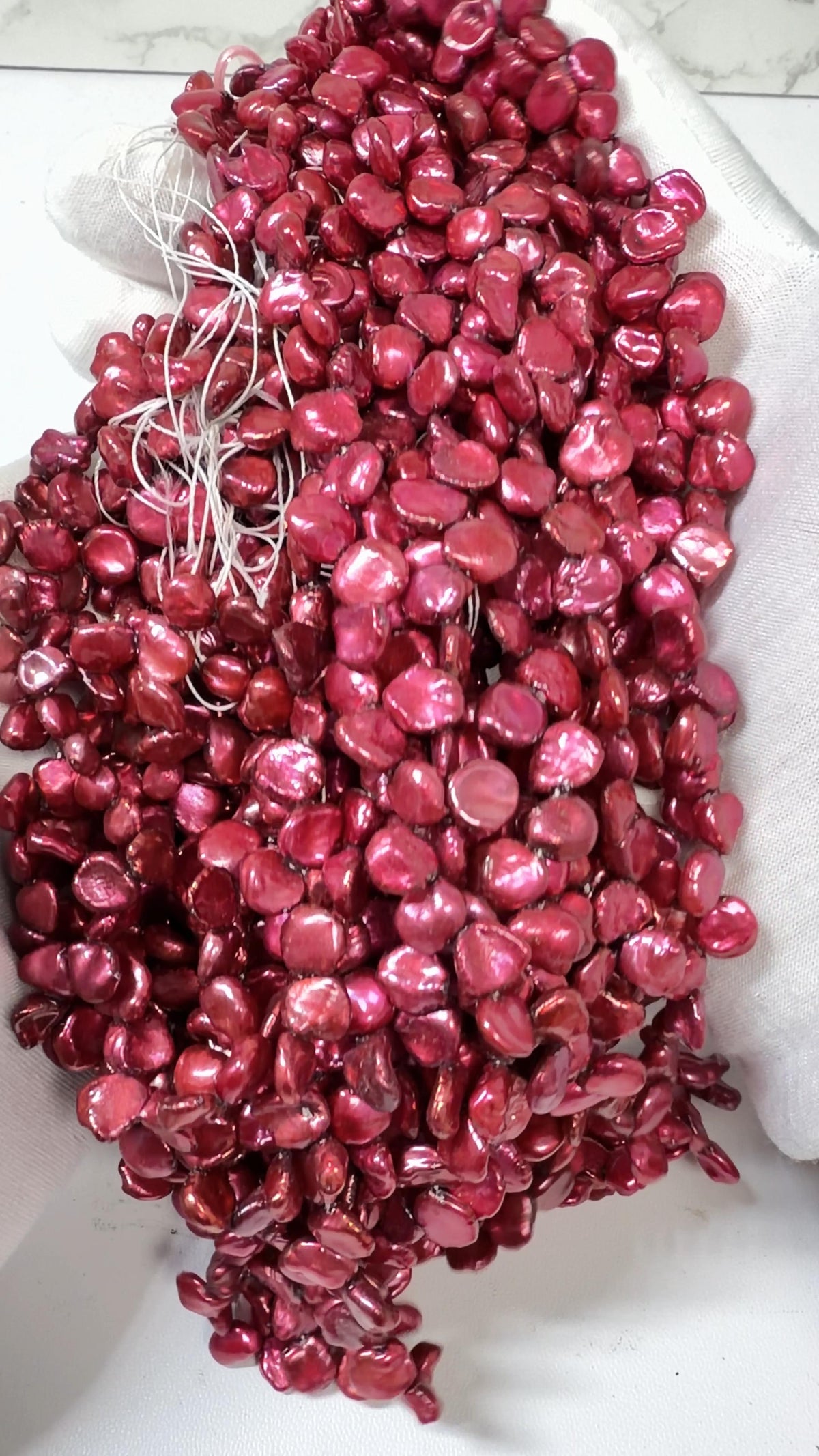 Raspberry Keshi pearl strands draped over a white gloved hand