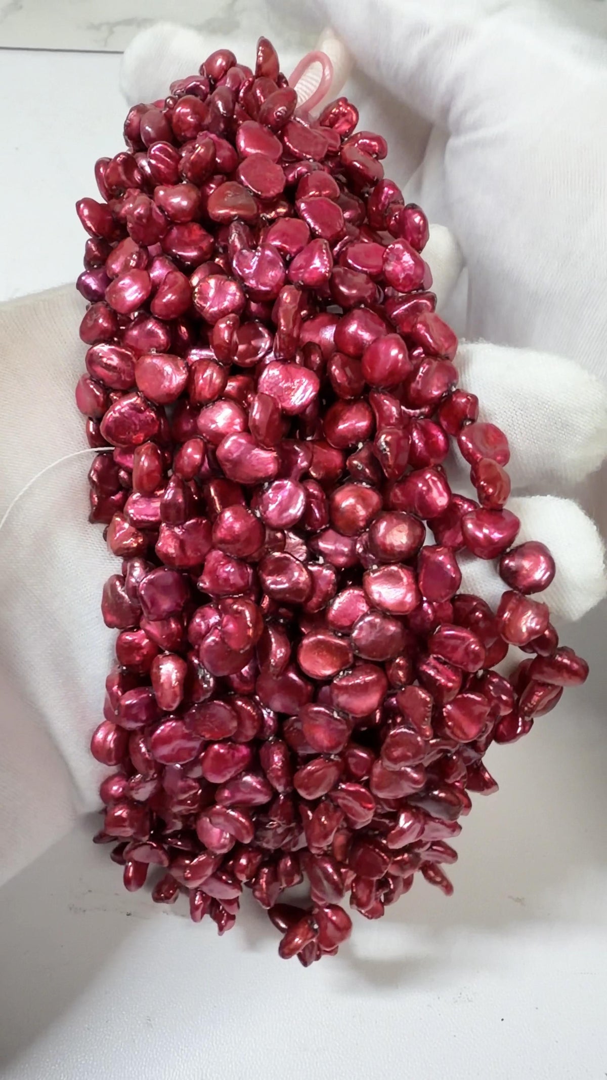 Raspberry Keshi pearl strands draped over a white gloved hand