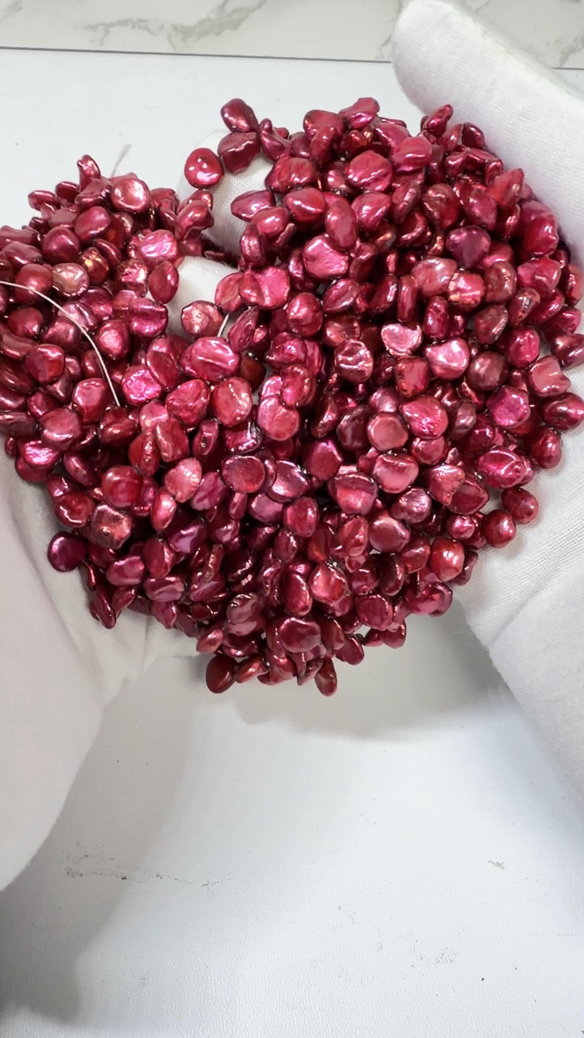 Raspberry Keshi pearl strands draped over a white gloved hand