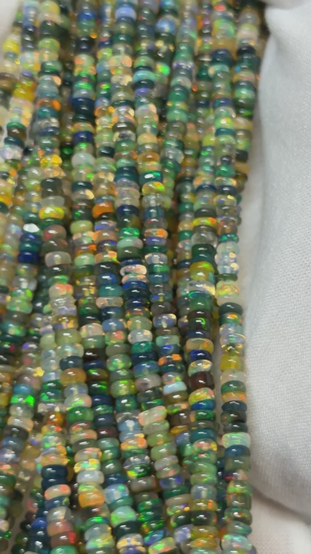 Video of strands of multi color opal beads on a white glove